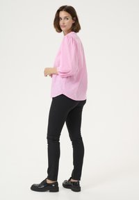 Blouse rose clair avec des manches bouffantes, texturée avec de petits motifs à pois, assortie à un jean skinny noir et des chaussures noires chunky.