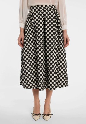 Schwarzer Midirock mit weißen Polka-Dots, getragen zu einer beigen Langarmbluse und beigen spitzen Schuhen mit schwarzen Schleifen.