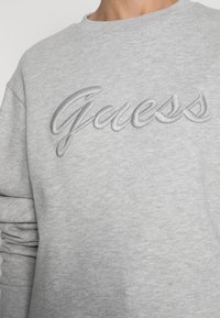 Grijze sweatshirt gemaakt van zachte stof met geborduurd "Guess" logo in een bijpassende grijze draad. Ronde halslijn en een relaxte pasvorm.