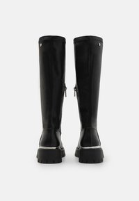 Botas negras hasta la rodilla, hechas de cuero suave, con cremallera lateral, suela de goma gruesa y un detalle plateado cerca del tacón.
