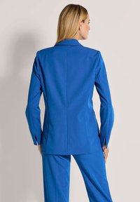Op maat gemaakte blauwe blazer met een soepele textuur, notch-kleppen en lange mouwen. Heeft een aansluitende pasvorm met zijsplitten.