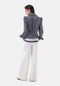 Bluse mit Marine-Muster und Puffärmeln sowie kontrastierenden blauen und beigen Akzenten, kombiniert mit hoch taillierten weißen weitgeschnittenen Hosen.