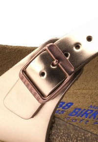 Sandale en cuir rose clair avec boucle métallique argentée. Elle possède une semelle intérieure en suede marron et un marquage bleu sur la plantille.