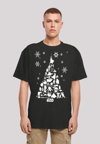 Melnā T-kreklā ir balts grafisks dizains ar Ziemassvētku eglīti, kas veidota no Star Wars varoņiem, ar sniegpārslām un "Star Wars" tekstu apakšā.