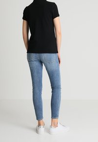 Chemise noire à manches courtes associée à un jean skinny bleu clair et des baskets blanches, mettant en valeur une coupe ajustée et une texture denim classique.