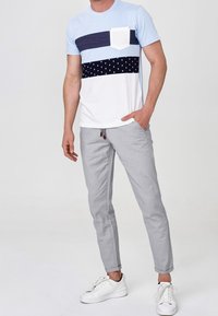 Ljusblå och marinblårandig t-shirt med en vit ficka, kombinerad med grå byxor och vita sneakers. Avslappnad bomullstyg, ledig passform.