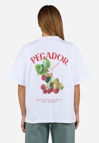 Fehér, rövid ujjú póló színes málna és levél grafikával, piros "PEGADOR." felirattal a hátoldalán. Laza fazon.
