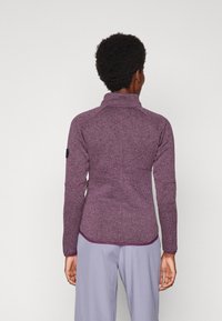 Fleecejersey-jacka i mörklila med hög krage, raglanärmar och en slimmad passform. Har en rund logopatch på vänster ärm.