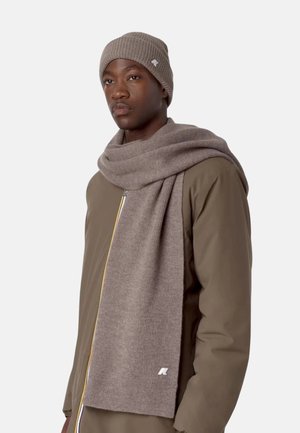 Bonnet en tricot brun et longue écharpe assortie avec texture côtelée. Portés sur une veste zippée marron avec un accent de fermeture éclair jaune.