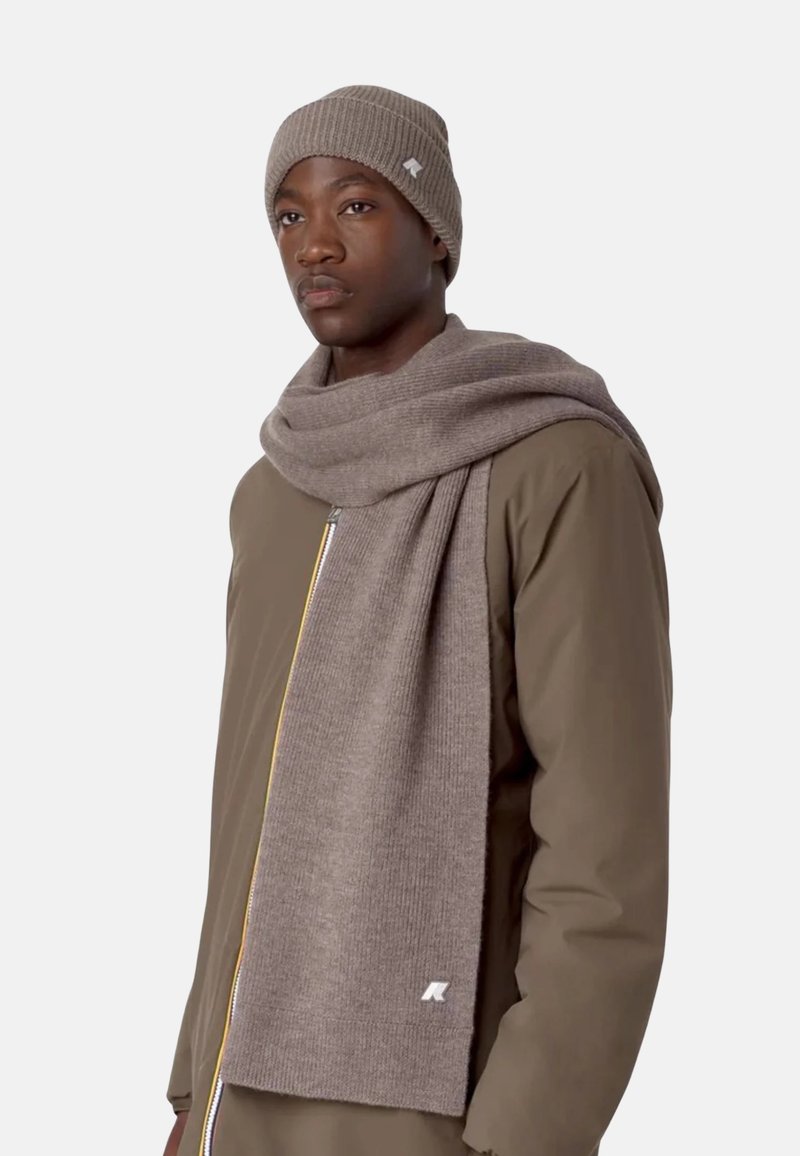 Bonnet en tricot brun et longue écharpe assortie avec texture côtelée. Portés sur une veste zippée marron avec un accent de fermeture éclair jaune.