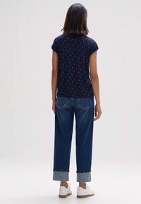 Merino lyhytnukkainen t-paita, jossa on valkoinen geometrinen kuvio, yhdistettynä leveisiin farkkuihin ja valkoisiin lenkkareihin, joissa on ruskea pohja.