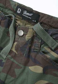 Pantaloni con motivo mimetico, coulisse verde, bottone metallico e etichetta Brandit che mostra la taglia M e il testo "Individual Wear".