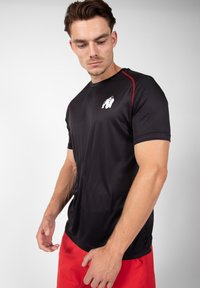 Zwarte sportieve t-shirt met rode accenten, gemaakt van een vochtregulerende stof. Bevat een gorilla-logo op de borst en heeft een aansluitend design.