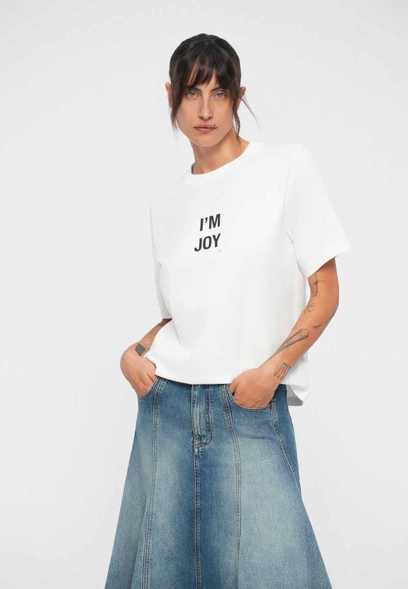 Vit kortärmad t-shirt med "I'M JOY" tryckt i svart. Matchad med en ljusblå denimkjol med en utsvängd form och fickor.