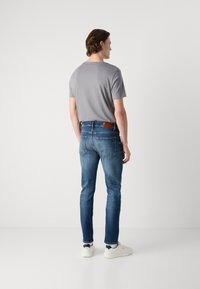 Tricou gri cu mânecă scurtă, asortat cu blugi slim-fit de culoare bleu închis, având o etichetă din piele maro pe talie. Modelul poartă adidași albi.