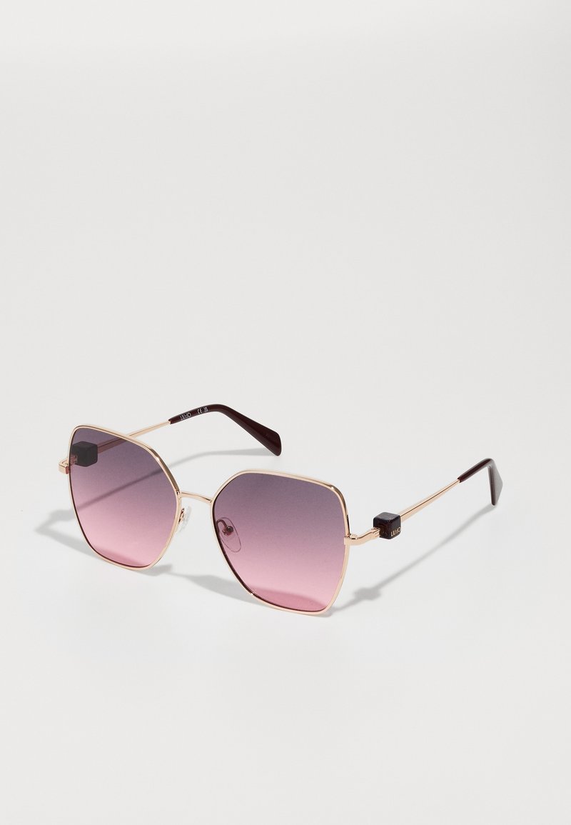 Octagonal sunglasses with a pink gradient lens; gold metal frame; black accents on temples; sleek design with textured details.