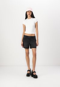 Crop top blanc à manches courtes, shorts en denim noir, talons plateforme noirs et casquette rose. Design simple avec une silhouette ajustée et des couleurs classiques.