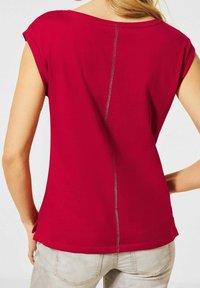 Röd kortärmad topp med lös passform, med en central söm på baksidan och subtila sömdekor. Mjuk, lätt tyg med en slät yta.