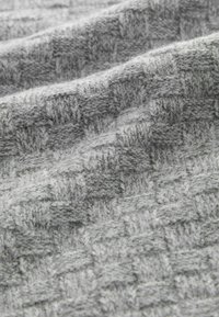 Un tejido gris texturizado presenta un patrón tejido con cuadrados elevados, mostrando una apariencia suave y acogedora. Las fibras crean una textura ligera y difusa.