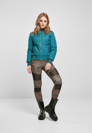 Teal quiltet bomberjakke med ribbede mansjetter, kombinert med leopardmønstrede leggings med meshpaneler. Sorte chunky hæler fullfører antrekket.
