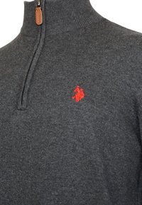 Suéter de punto gris oscuro con una cremallera de cuarto y un pequeño logo bordado en rojo de un jugador de polo en el pecho.