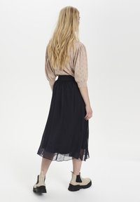 Light pink, patterned blouse with puffed sleeves, paired with a flowing, dark navy skirt. Chunky beige ankle boots complete the look.