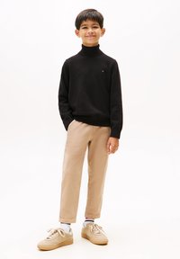 Maglione nero a collo alto, chinos beige e sneakers beige. Il maglione ha un piccolo logo sul petto; i pantaloni hanno un design a gamba dritta.