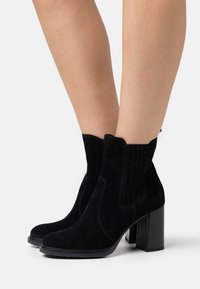 Svarta mocka ankelstövlar med rund tå, elastiska sidopaneler och en kraftig blockklack. Designen har vertikala sömnadsdetaljer.