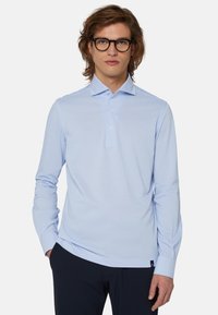 Svetlo modra dolga majica s polo ovratnikom, s tremi gumbi in majhnim logotipom na robu. Gladek, mehak tekstil.