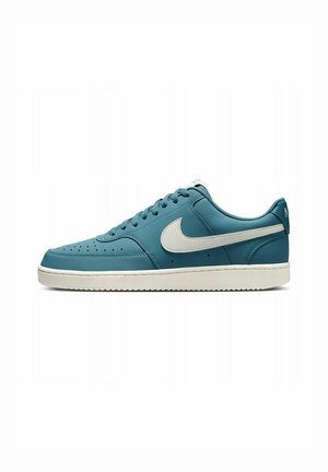 Lage blauwe sneaker met witte Nike-swoosh en witte zool, zijaanzicht op een effen witte achtergrond.