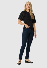 T-shirt nera con maniche a sbuffo testurizzate, abbinata a jeans skinny blu scuro e ballerine nere. Design semplice e aderente con una texture liscia.