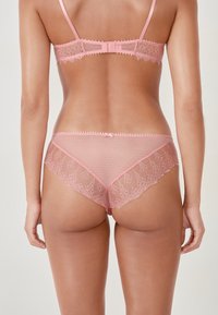 Rosa Spitzen-BH und Slip-Set mit einem strukturierten Spitzenmuster, gepunktetem Design, gewellten Kanten und einem kleinen Schleifenakzent auf der Rückseite.