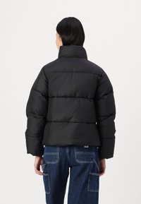 Schwarze Pufferjacke mit hohem Kragen, die horizontale, gesteppten Abschnitte aufweist. Hergestellt aus einem glatten Material, hat sie ein verkürztes Design und eine lockere Passform.