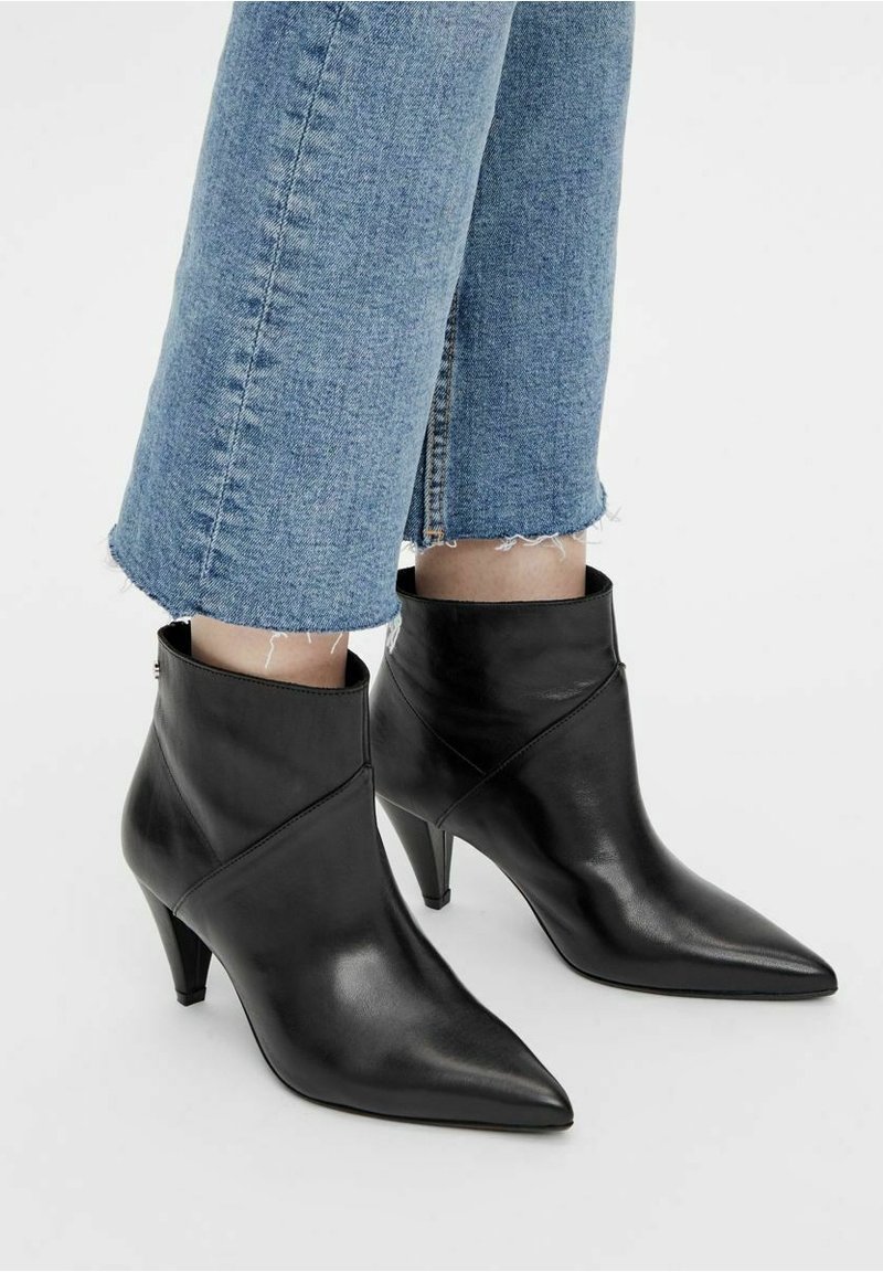 Bottines noires à bout pointu avec talons moyens portées avec un jean bleu court sur fond clair.