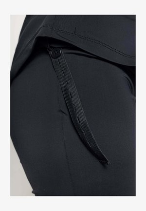 Zwarte broek met een gladde textuur, een zijknoop en een zichtbare banddetail langs de naad. De stiksels zijn netjes en consistent.