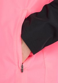 Veste rose vif avec une poche zippée. Manche noire avec une texture lisse. Présente un design épuré et un contraste de couleurs.