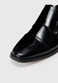 Schwarzer lacklederner Dressschuh mit elegantem Design, spitz zulaufender Zehenpartie und zwei breiten Riemen für eine sichere Passform. Der glänzende Abschluss erhöht die visuelle Attraktivität.