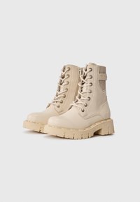 Beige lærstøvler til ankler med kraftige gummisåler, runde tæer, snører og lynlås på siden. Inkluderer en mærketabs på bagsiden.