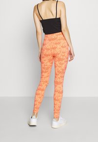 Högmidjade leggings i klargul med blommönster, gjorda av elastiskt material, ihopparade med en svart linne och vita sneakers.