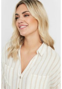 Vit skjorta med vertikala beige ränder, med två bröstfickor och ett lätt, texturerat tyg.