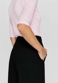 Roze getailleerde top met driekwartmouwen, gecombineerd met zwarte hoge taille broeken. De broeken hebben zijzakken en een gladde textuur.