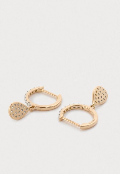 Zelta tonis auskari gredzenu veidā ar teksturētu, perforētu asaras formas piekariņu. Malās ir skaidri rhinakmeņi papildu detaļām.