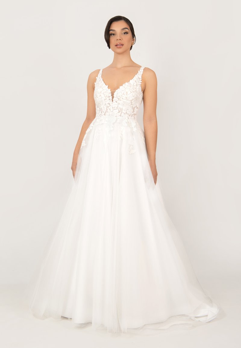 Weißes Kleid mit V-Ausschnitt, floraler Spitzenoberteil und einem fließenden Rock aus transparentem Material. Die Träger sind zart und strukturiert.
