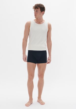 Weiße gerippte Tanktop, kombiniert mit schwarzen Boxershorts. Das Outfit zeichnet sich durch ein enges Design mit einer glatten Textur und minimaler Detailierung aus.