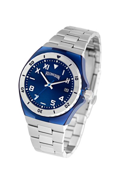 Reloj azul con cara redonda, marcadores de hora plateados y una correa de acero inoxidable. Presenta un bisel azul y una pantalla de fecha a las 3 en punto.
