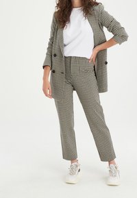 Černobílý houndstooth blazer a odpovídající kalhoty s bílým tričkem. Kombinováno s bílými a šedými teniskami. Hladká látka, přiléhavý střih.