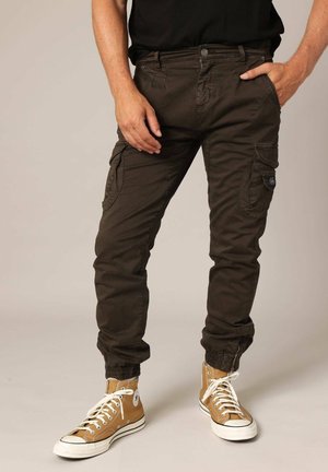 Donkergroene cargobroek met meerdere zakken, aangesloten cuffs en een gladde, duurzame stof. Gekomplementeerd met tan hoge sneakers.