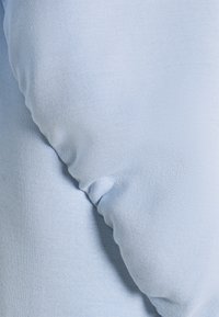 Tela de algodón azul claro que muestra una textura suave con detalles fruncidos, creando una apariencia acolchada y suave. La vista en primer plano resalta la costura.