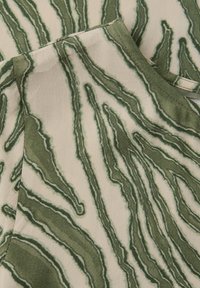 Gros plan sur un tissu avec un motif abstrait de rayures ondulées vertes et beiges, montrant des bords pliés et un col plié.