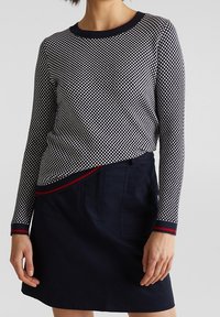 Granatowa i biała koszula w kratę z długim rękawem oraz okrągłym dekoltem, z czerwono-białymi paskami, w połączeniu z ciemnogranatową spódnicą.